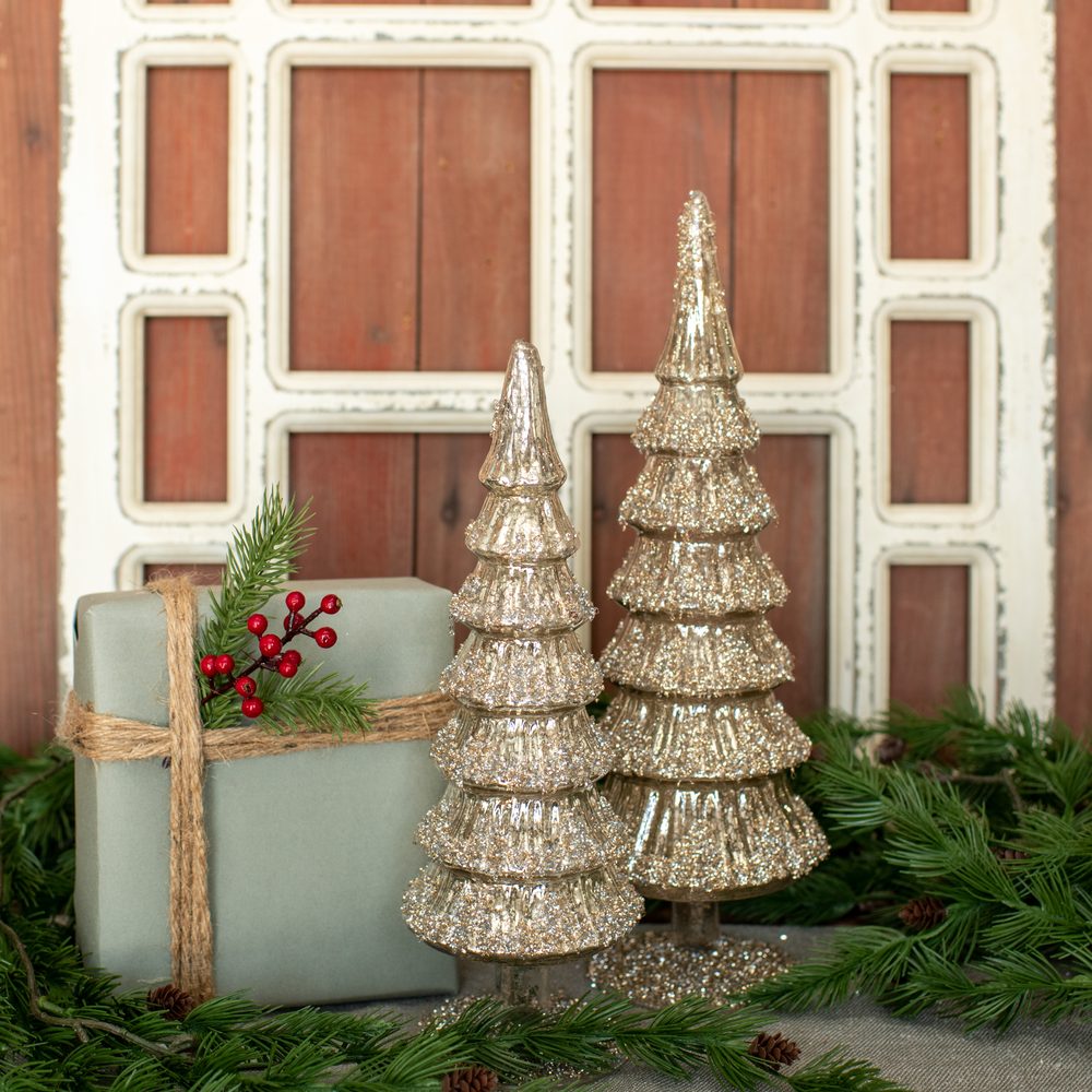Gold mercury-glass trees and a wrapped gift on pine boughs before an old red cabinet door