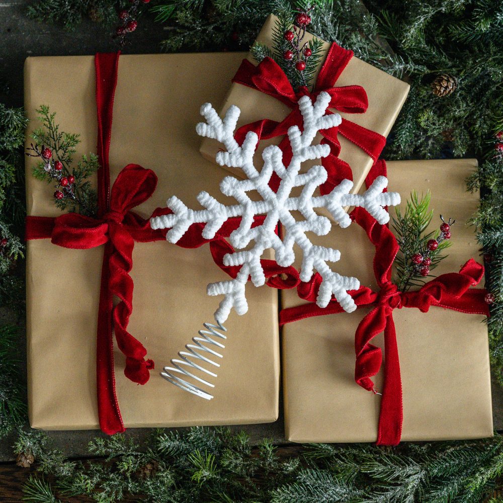 White snowflake tree topper on kraft-wrapped gifts tied with red velvet ribbon
