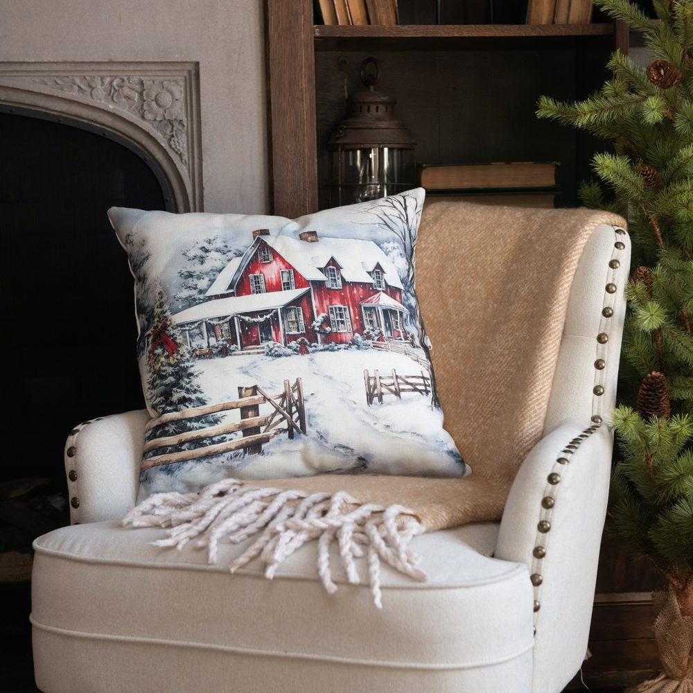 White tufted chair with a red-barn snow scene pillow and cream throw by a fireplace